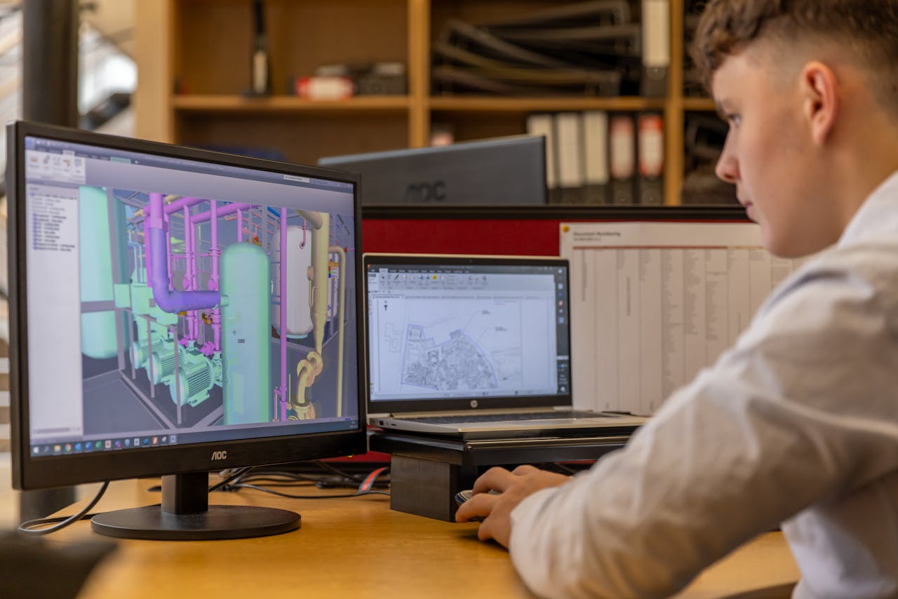 Engineer working with CAD software on dual monitors in an office setting.